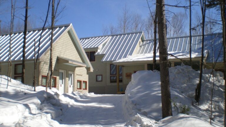 The Poplar Falls Hut with tan wood siding and a metal roof in winter. A cross country ski trail is in the foreground.