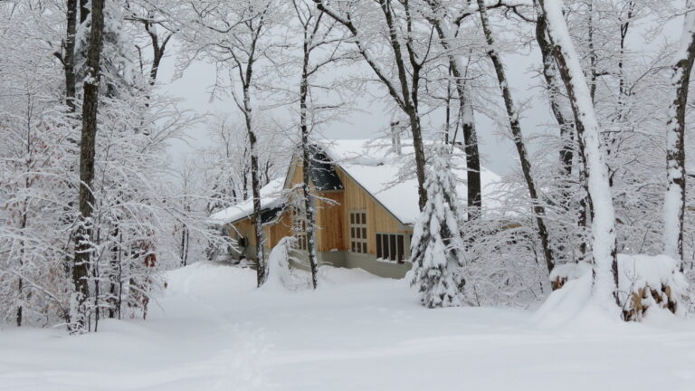 Image of the Stratton Brook Hut with wood sides after a snowfall with snow in the trees.