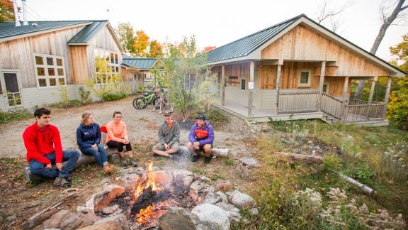 A group hangs around a firepit outdoors at Stratton Brook Hut.