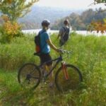 image of two mountain bikers looking over a pond with mountains in the background